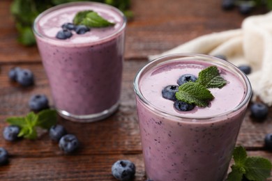 Photo of Glasses of blueberry smoothie with mint on wooden table, closeup