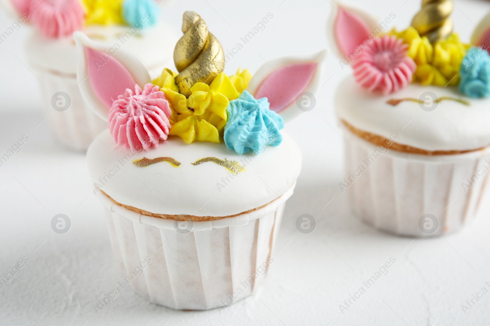 Photo of Cute sweet unicorn cupcakes on white table, closeup