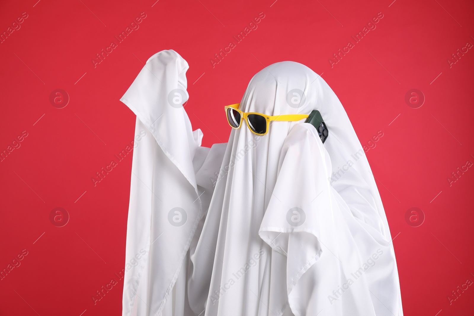 Photo of Person in ghost costume and sunglasses talking on smartphone against red background