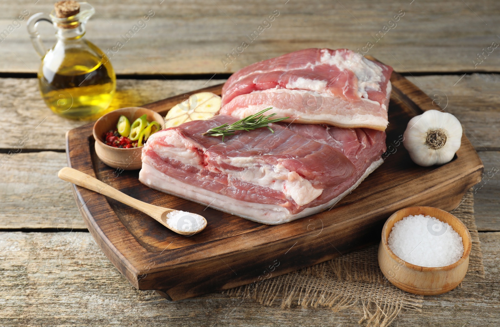 Photo of Pieces of raw pork belly, salt, oil, garlic and rosemary on wooden table