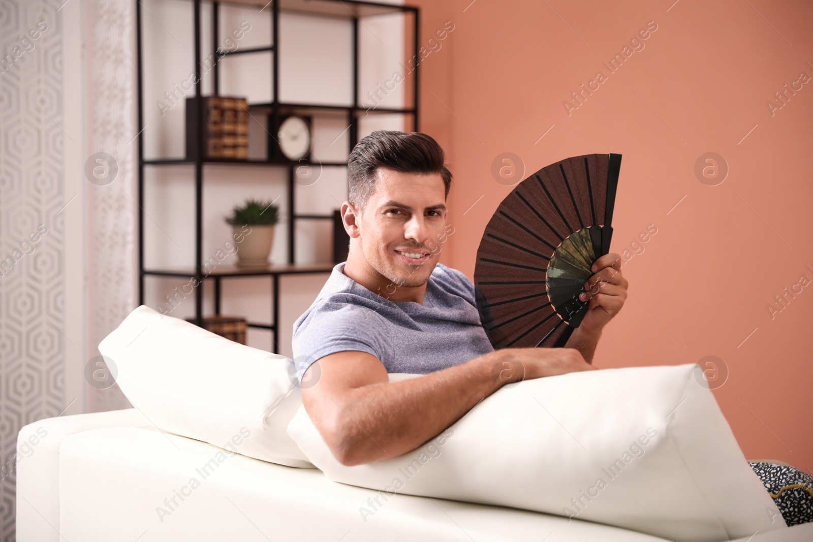 Photo of Man with hand fan sitting on sofa. Summer season