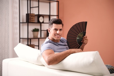 Photo of Man with hand fan sitting on sofa. Summer season