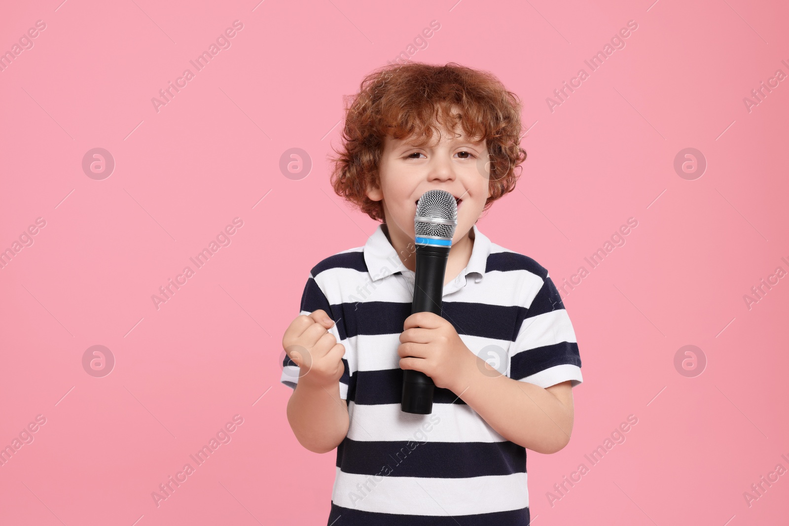 Photo of Cute little boy with microphone singing on pink background