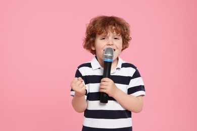Photo of Cute little boy with microphone singing on pink background