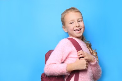 Happy little girl with backpack on light blue background. Space for text