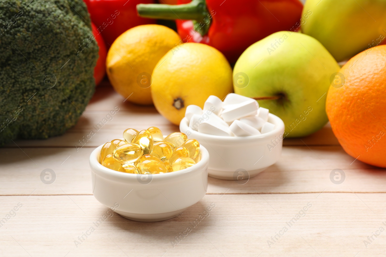 Photo of Dietary supplements. Bowls with different pills near food products on light wooden table, closeup