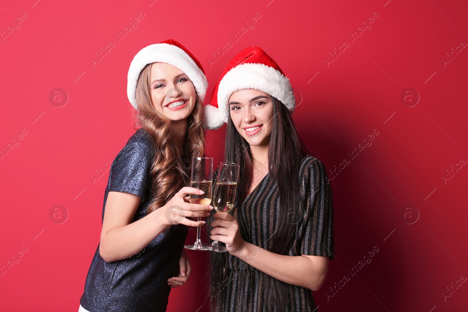 Photo of Beautiful young women in Santa hats with glasses of champagne on color background. Christmas celebration