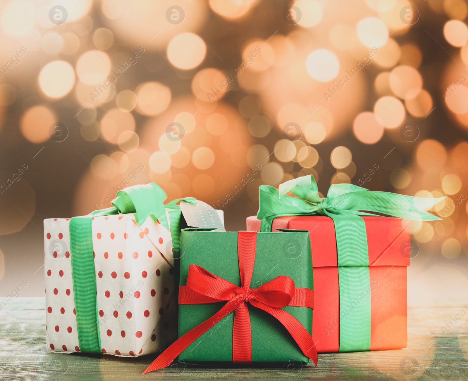 Image of Christmas gift boxes on wooden table against blurred background, bokeh effect