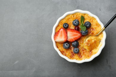 Delicious creme brulee with berries and mint in bowl served on grey table, top view. Space for text