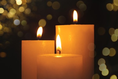Burning candles on dark background with blurred lights, closeup. Bokeh effect