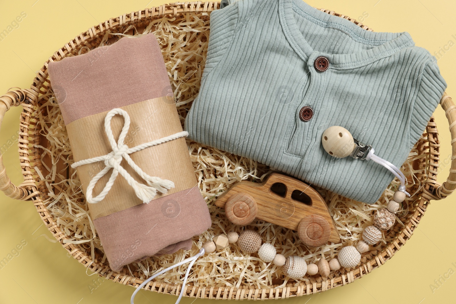 Photo of Different baby accessories and clothes in wicker basket on yellow background, top view