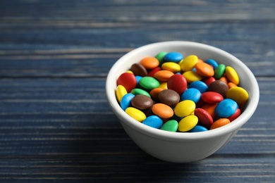 Bowl with colorful candies on wooden background. Space for text