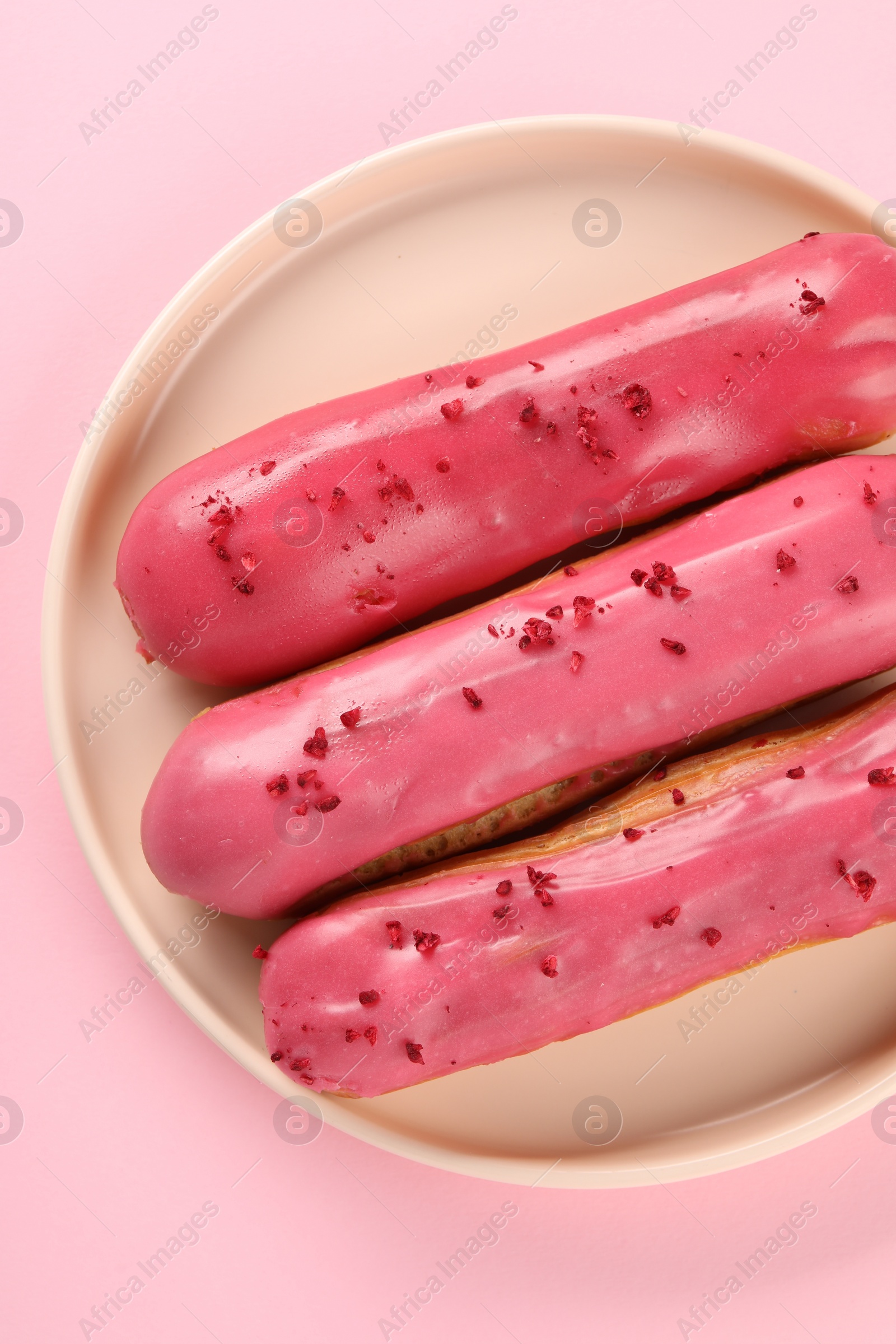 Photo of Delicious eclairs covered with glaze on pink background, top view