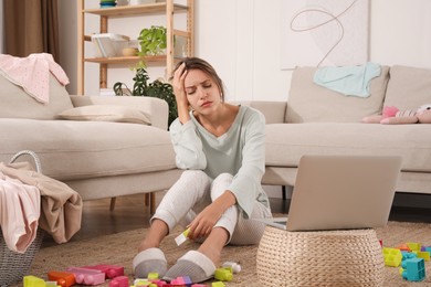 Photo of Tired young mother sitting on floor in messy living room