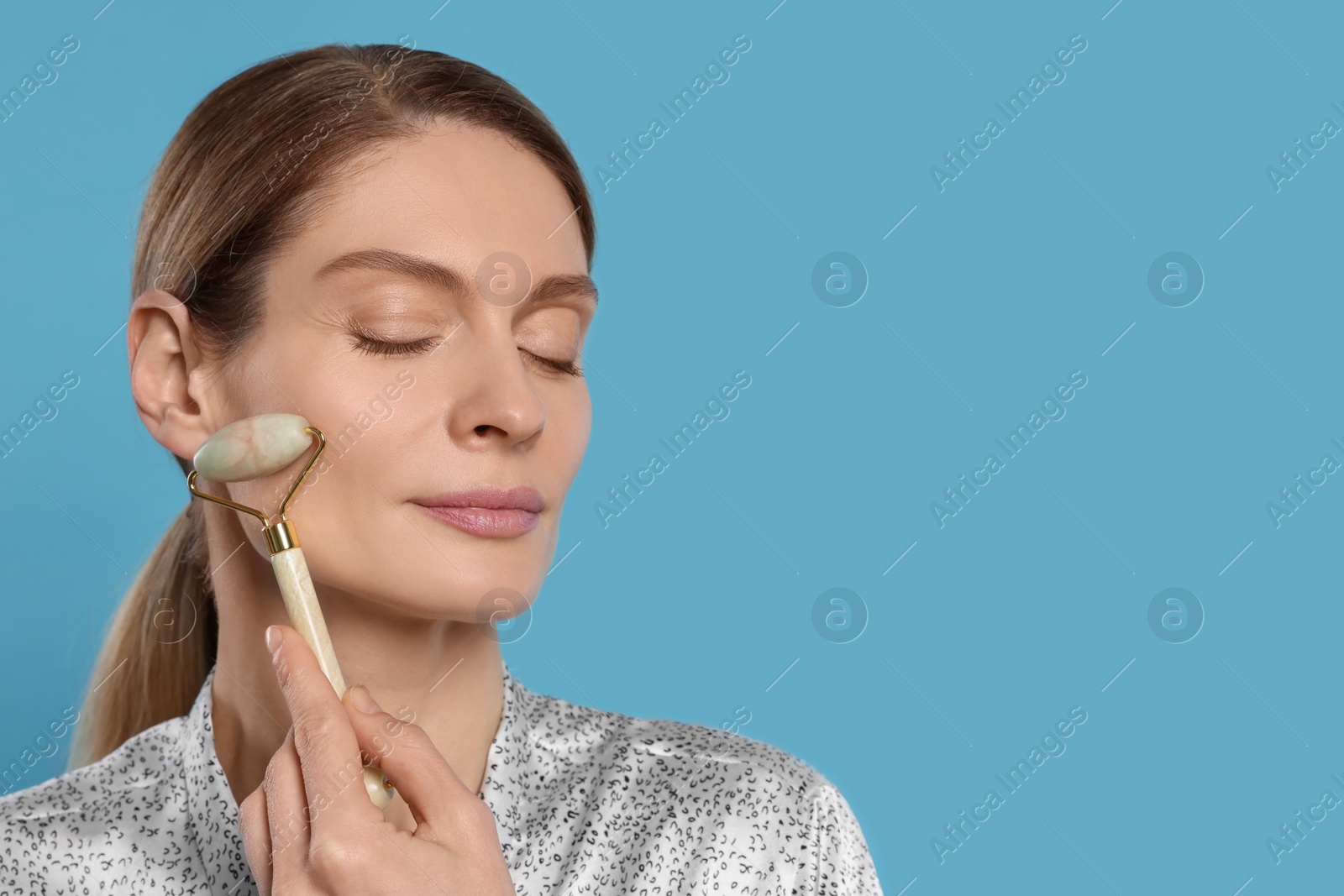 Photo of Woman massaging her face with jade roller on turquoise background. Space for text
