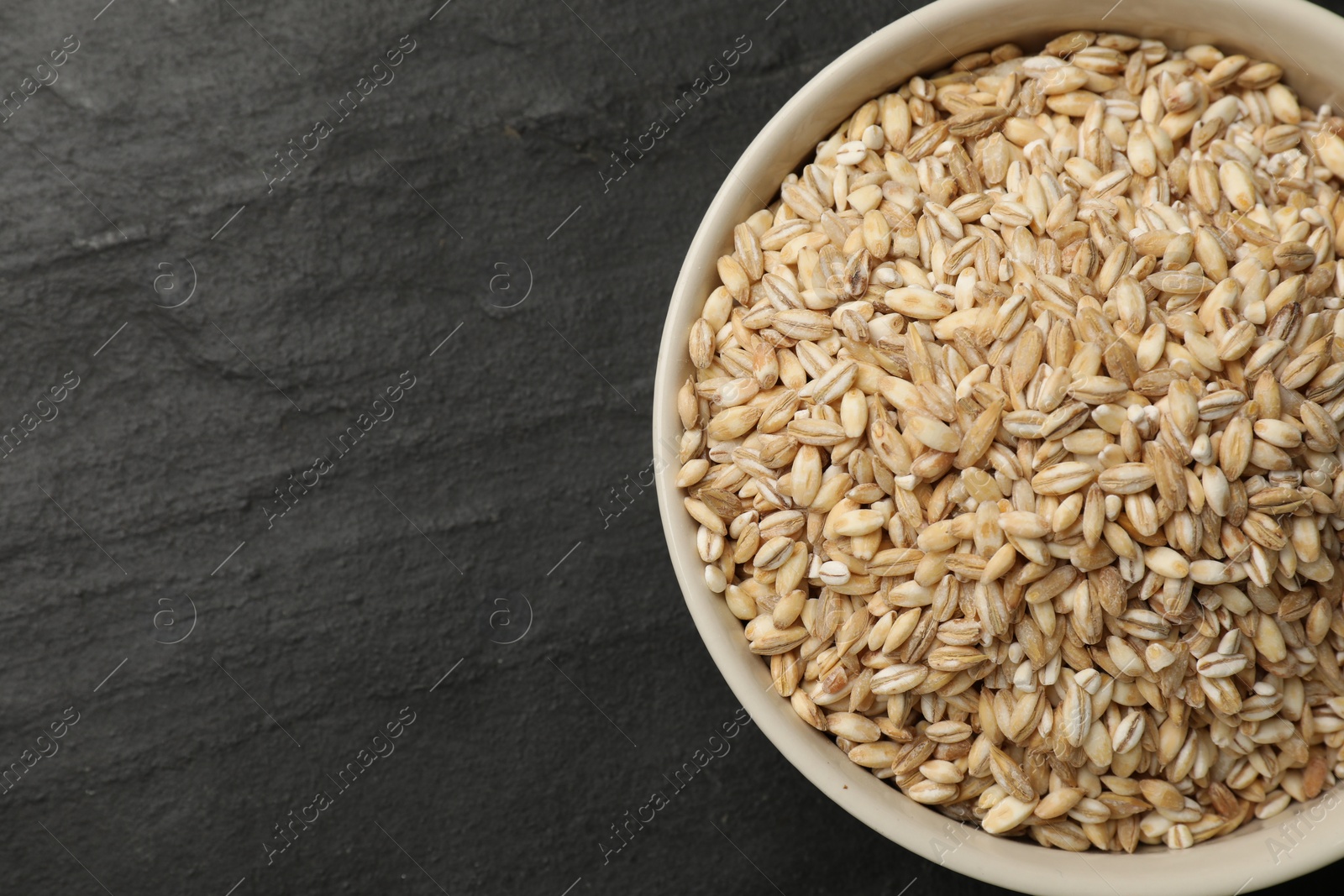 Photo of Dry pearl barley in bowl on dark gray table, top view. Space for text
