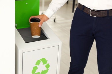 Photo of Young man throwing coffee cup into recycling bin in office, closeup