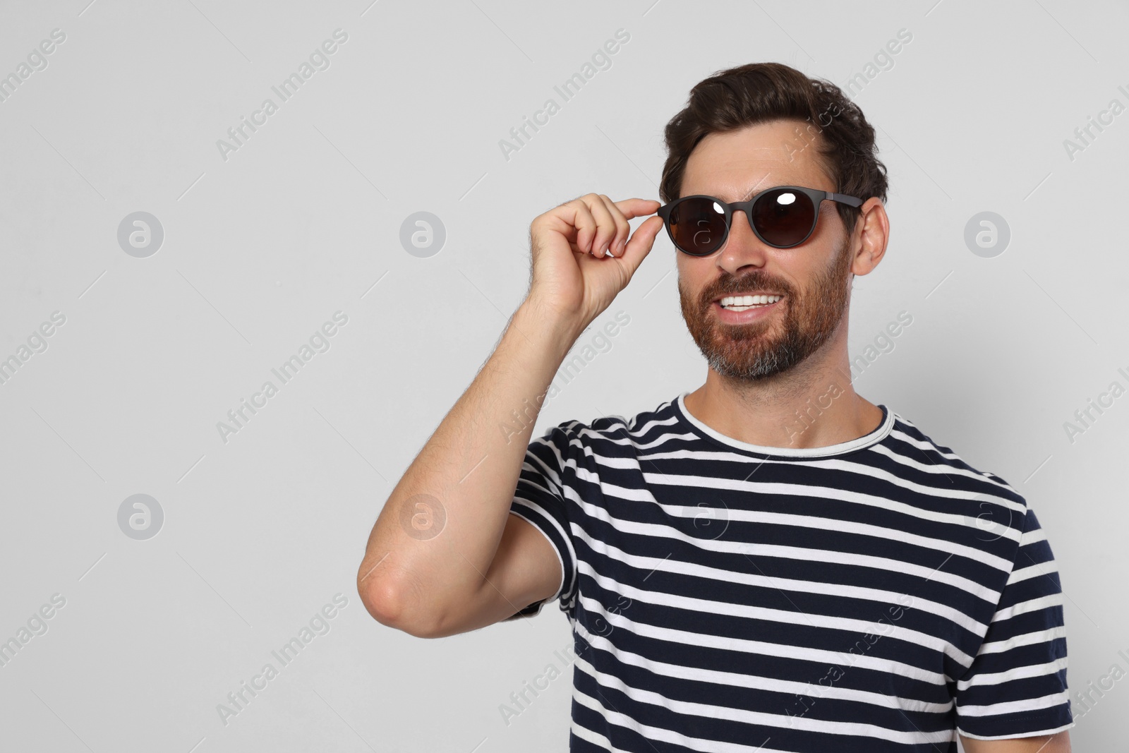 Photo of Portrait of smiling bearded man with stylish sunglasses on light grey background. Space for text