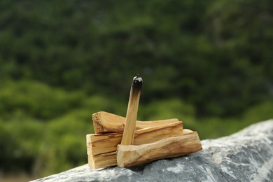 Burning palo santo stick on stone surface outdoors, closeup