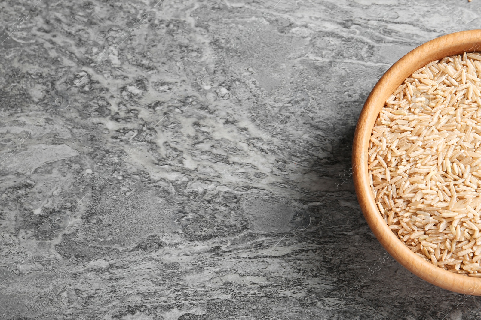 Photo of Brown rice in wooden bowl and space for text on grunge background, top view