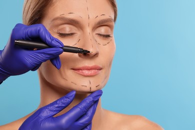Photo of Doctor with marker preparing patient for cosmetic surgery operation on light blue background, closeup. Space for text