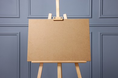 Wooden easel with blank board near grey wall indoors, closeup