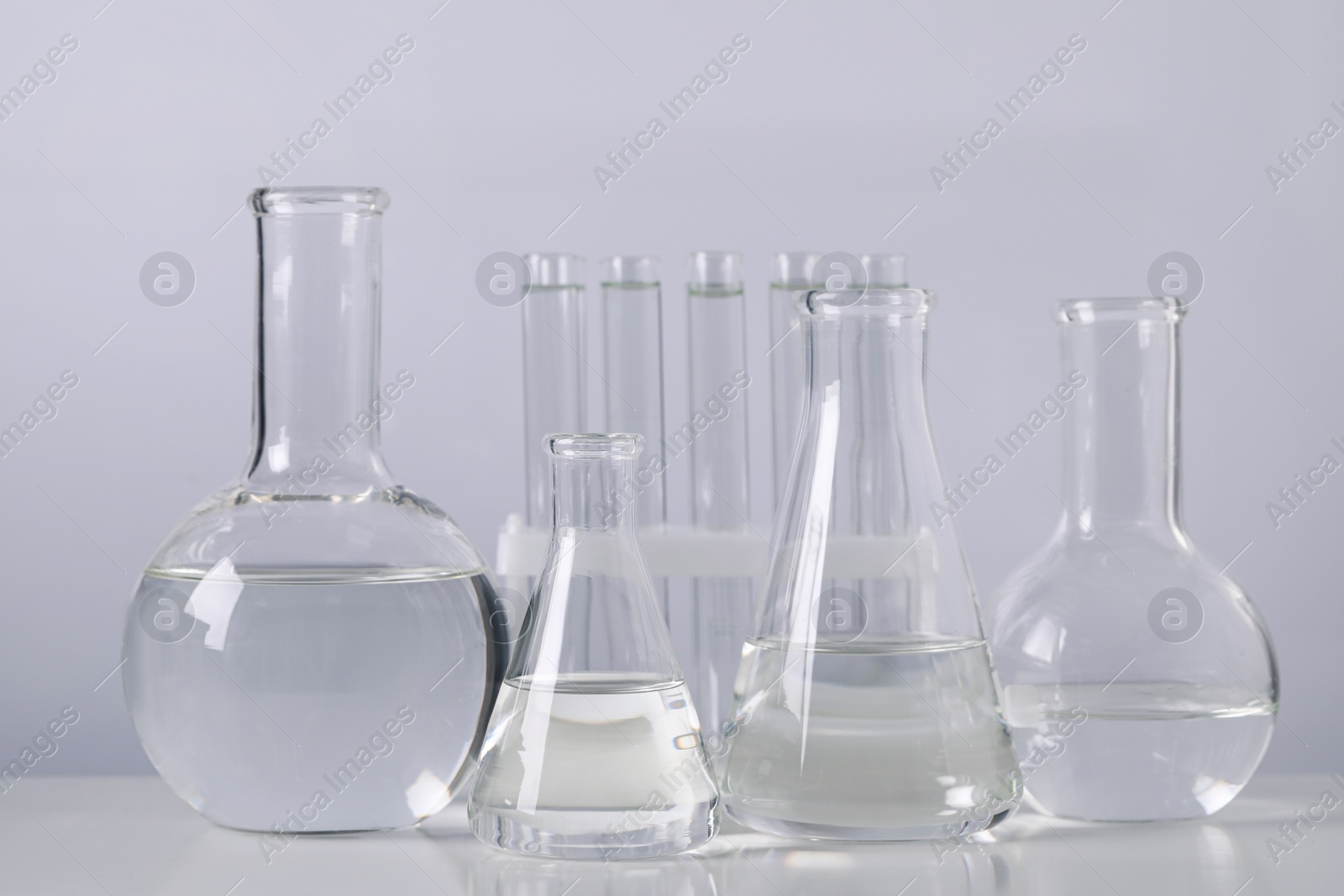 Photo of Different laboratory glassware with transparent liquid on table against light background