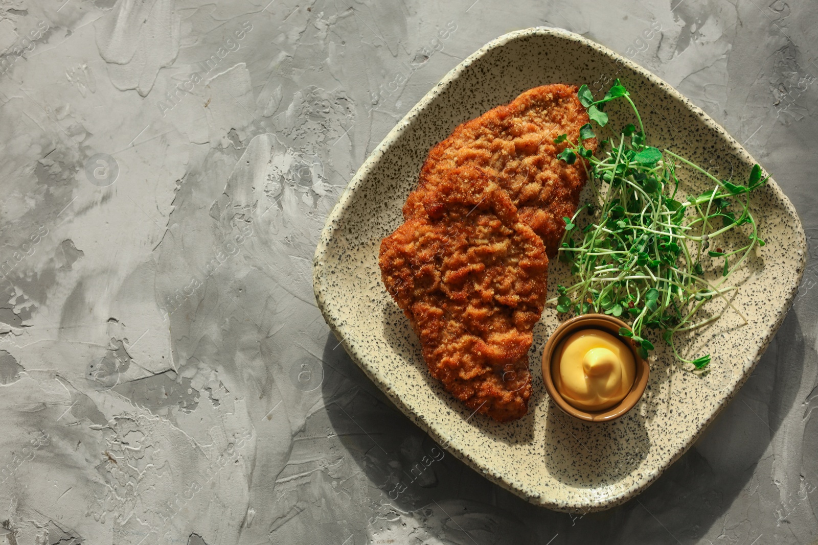 Photo of Tasty schnitzels served with sauce and microgreens on grey textured table, top view. Space for text