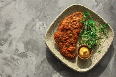 Tasty schnitzels served with sauce and microgreens on grey textured table, top view. Space for text