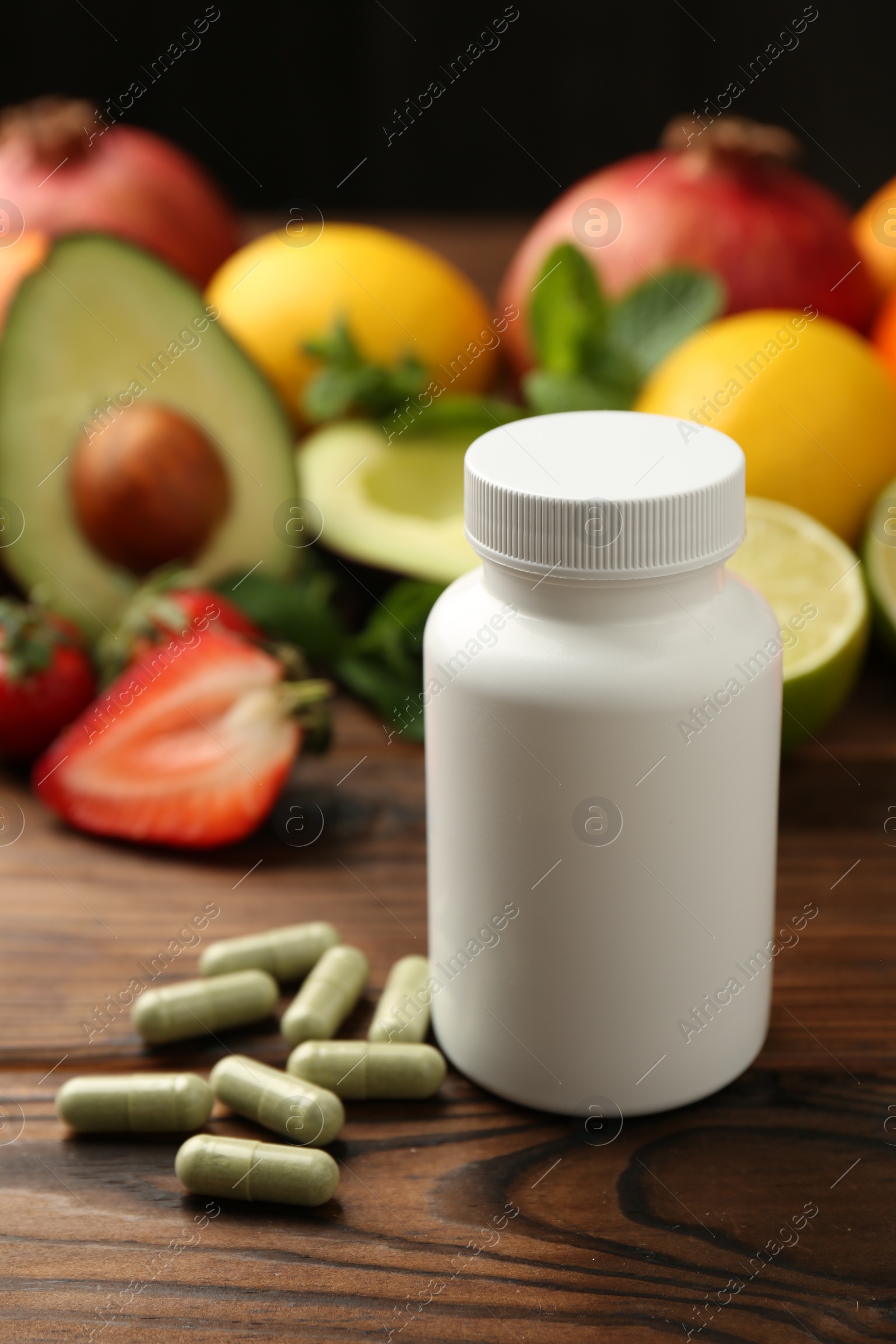 Photo of Vitamin pills, bottle and fresh fruits on wooden table