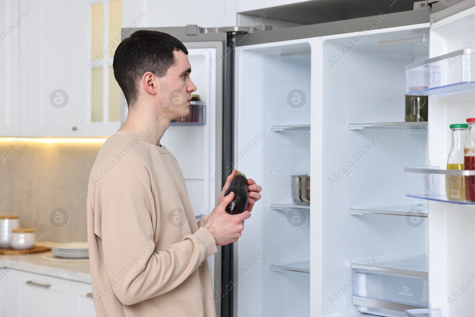 Photo of Upset man with eggplant near empty refrigerator in kitchen