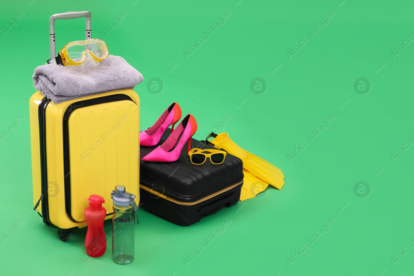 Photo of Suitcases, bottles and beach accessories on green background, space for text. Summer vacation