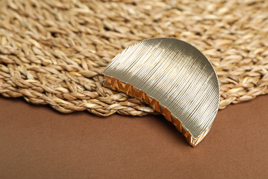 Stylish hair clip and wicker mat on brown background