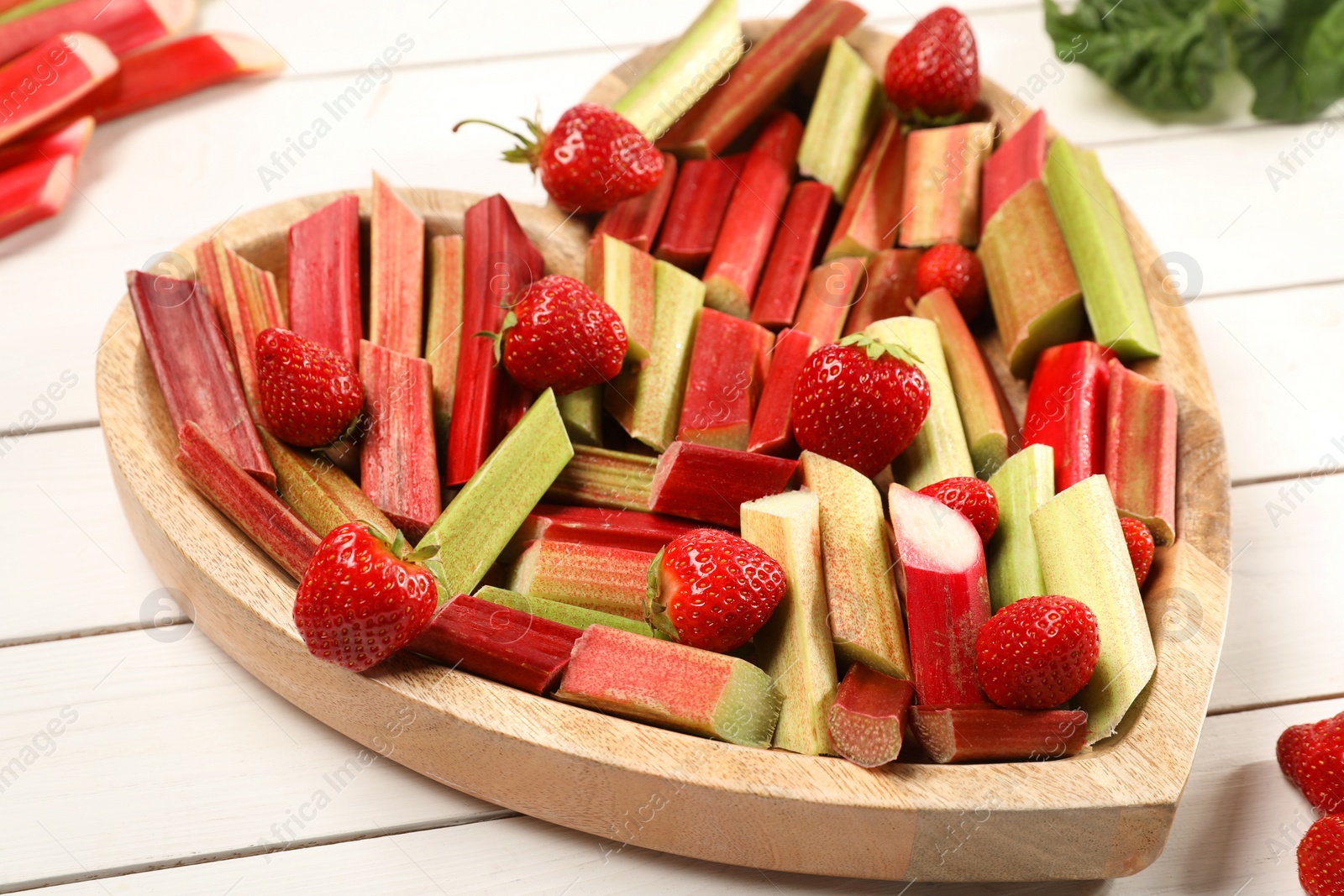 Photo of Cut fresh rhubarb stalks and strawberries on white wooden table, closeup