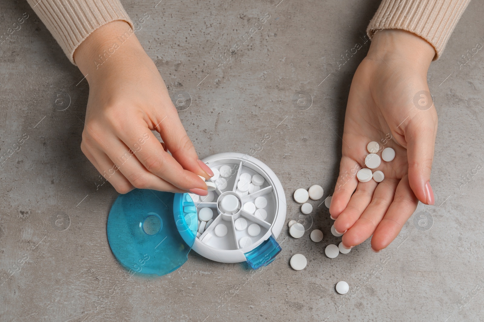 Photo of Woman putting pill into plastic box at grey table, top view