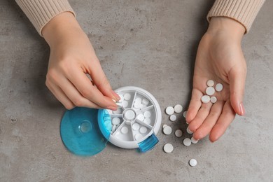 Woman putting pill into plastic box at grey table, top view