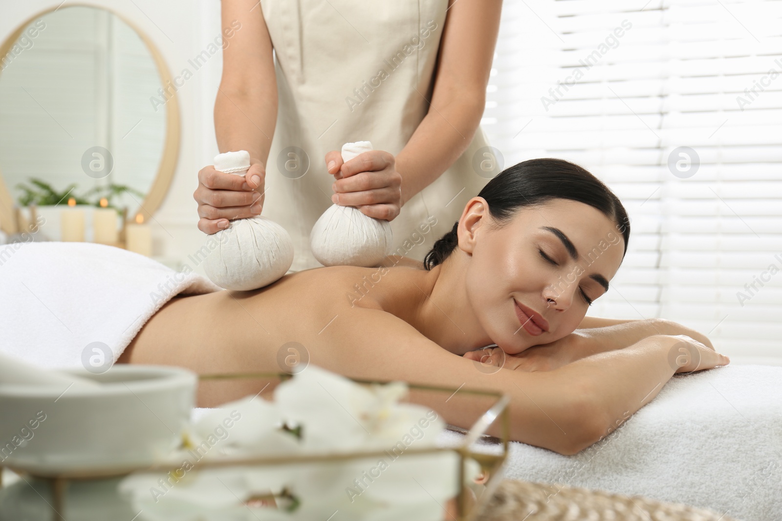 Photo of Young woman receiving herbal bag massage in spa salon