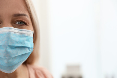 Photo of Mature woman wearing medical mask at home, closeup view with space for text. Dangerous virus