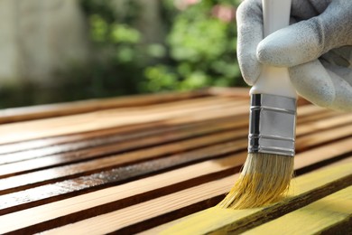 Worker painting wooden surface with yellow dye outdoors, closeup. Space for text