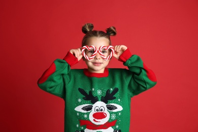 Photo of Cute little girl in Christmas sweater and party glasses on red background