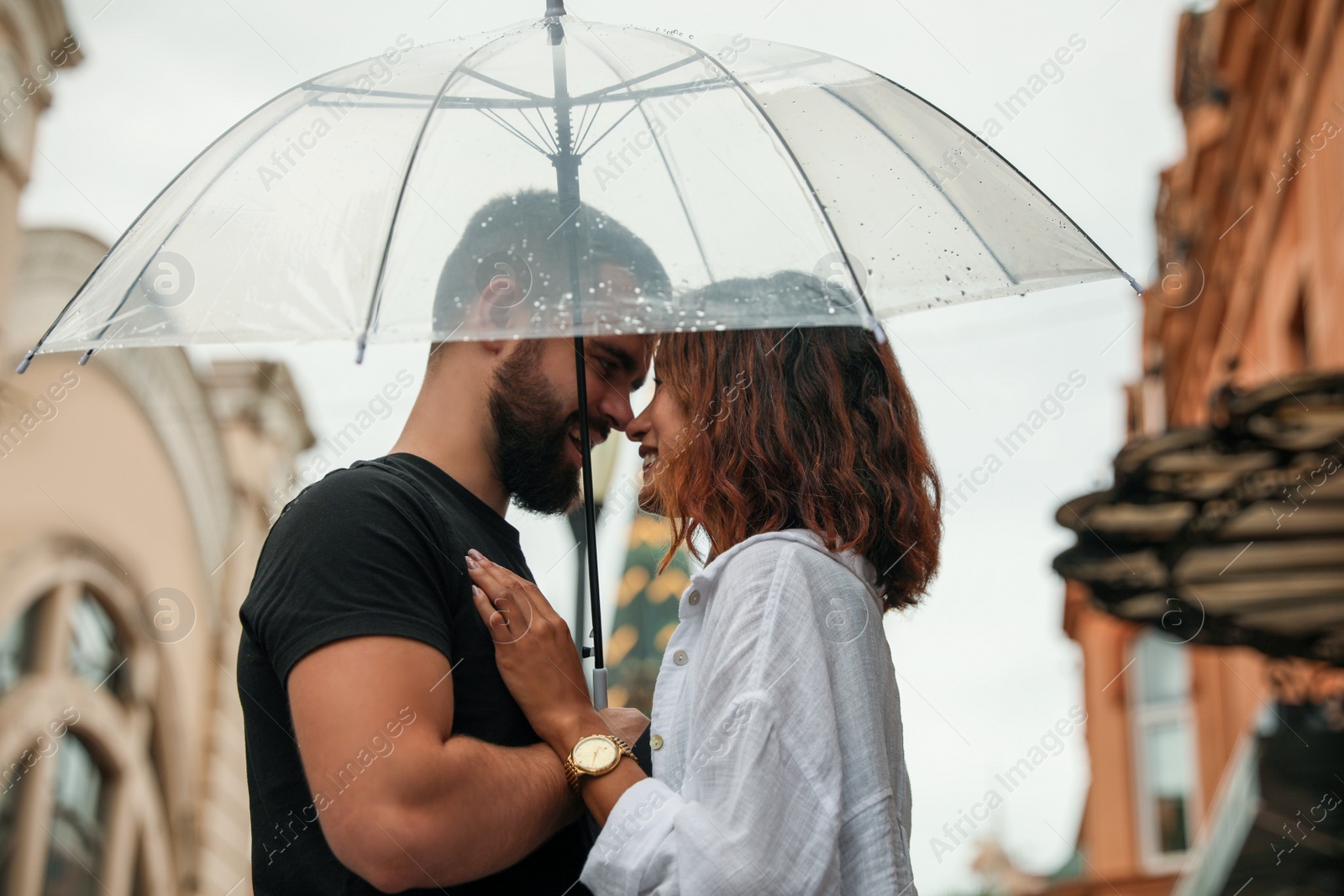 Photo of Young couple with umbrella enjoying time together under rain on city street