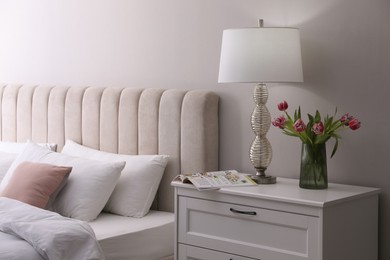 Stylish lamp, flowers and magazine on bedside table indoors. Bedroom interior elements