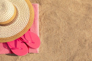 Beach towel with slippers and straw hat on sand, top view. Space for text