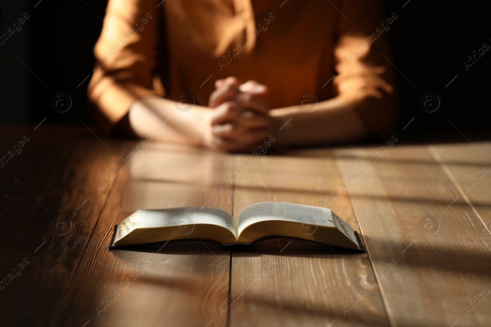 Photo of Religious woman praying over Bible at wooden table indoors, focus on book