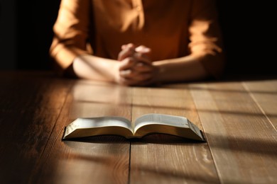 Photo of Religious woman praying over Bible at wooden table indoors, focus on book