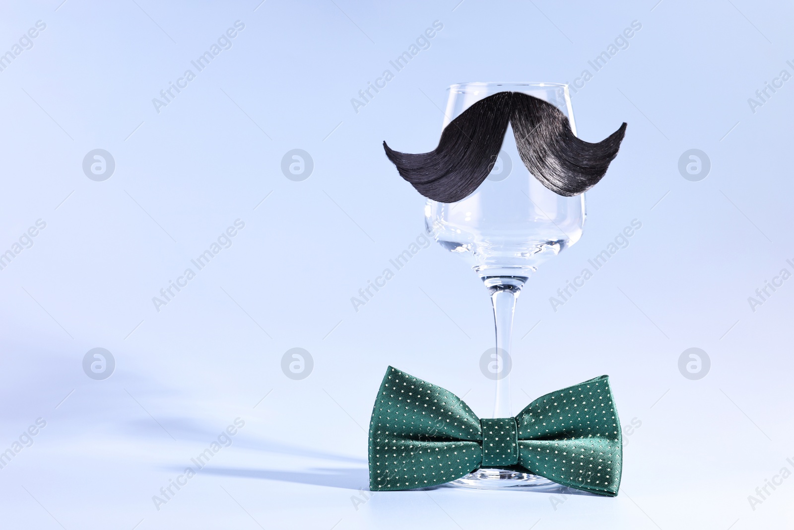 Photo of Man's face made of artificial mustache, bow tie and wine glass on light blue background. Space for text