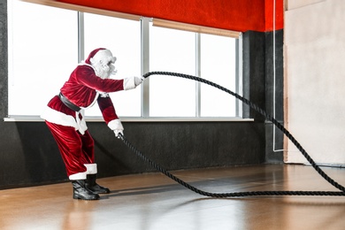 Young Santa Claus training with ropes in modern gym