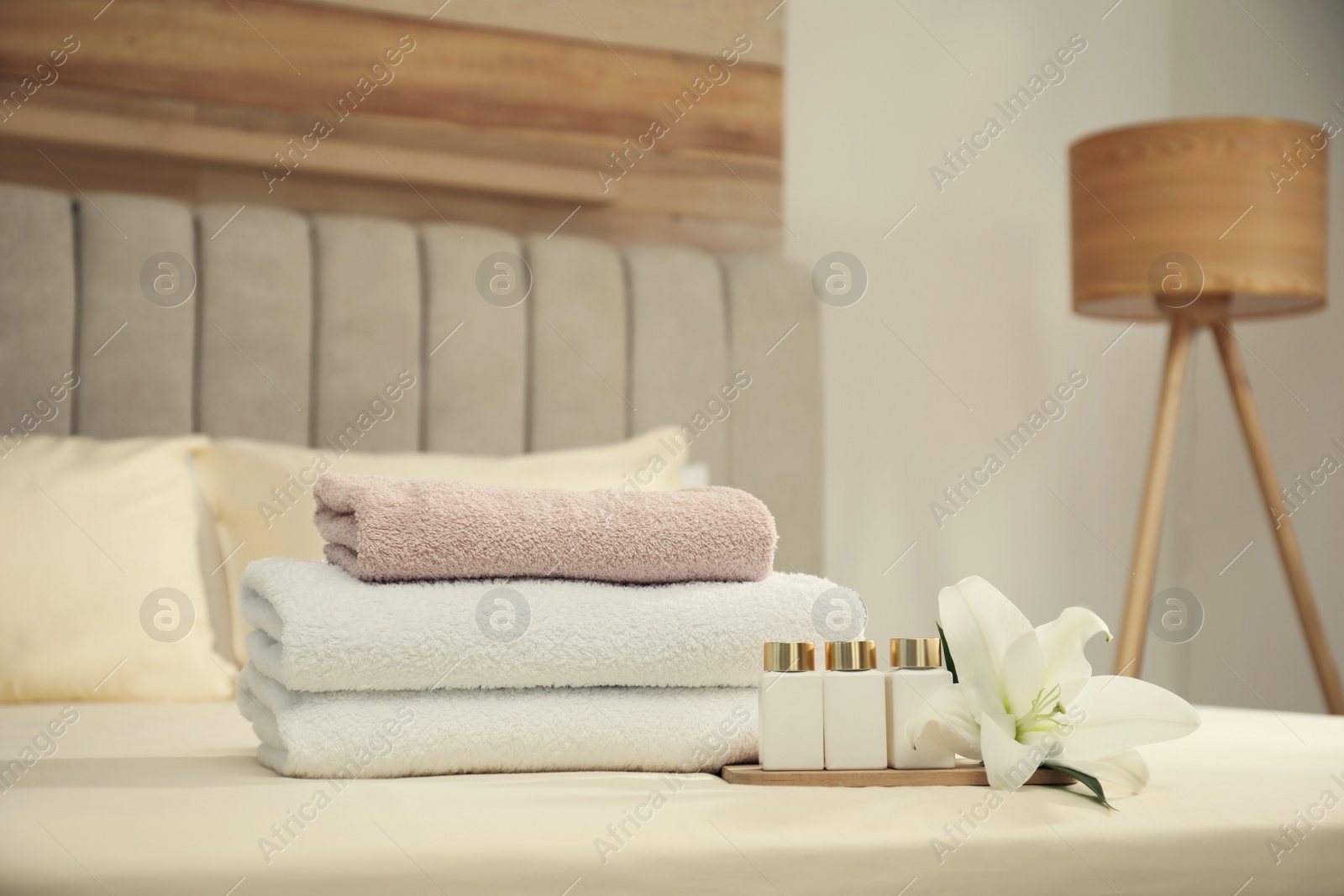 Photo of Stack of clean towels, flower and shampoo bottles on bed indoors. Space for text