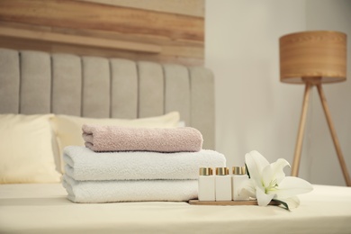 Stack of clean towels, flower and shampoo bottles on bed indoors. Space for text