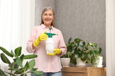 Happy housewife with plant mister near green houseplants at home
